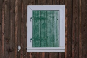 a window with green shutters on a wooden wall